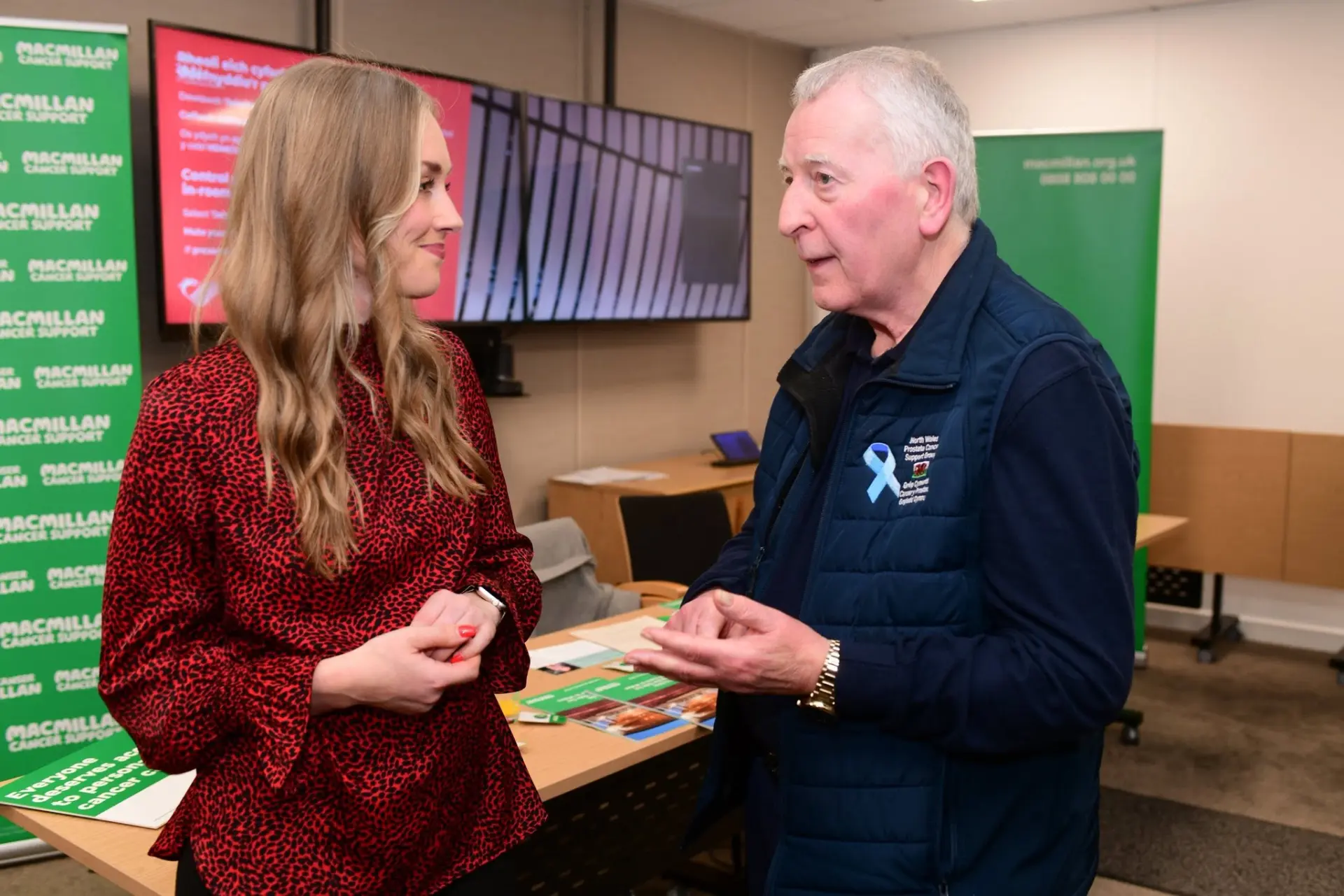 A group volunteer speaking with a visitor beside Macmillan Cancer Support banners
